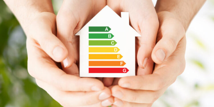 energy saving, real estate and family home concept - closeup of couple hands holding white paper house with energy efficiency rating