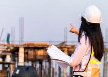 Construction Engineering Asian woman civil engineer paper plan building architect wearing white safety helmet look at the construction site.