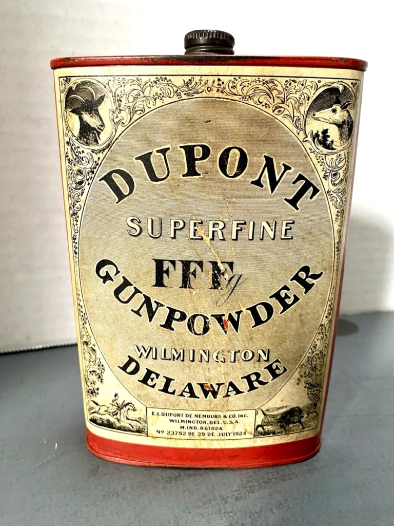Antiguos envases de cartón o metal para pólvora de la marca DuPont, con la inscripción «Superfine FF», el nombre de la empresa E.I. DuPont de Nemours & Co. Inc., y la ubicación Wilmington, Delaware, EE. UU. En la etiqueta se aprecia la fecha «DE29DEJULY1924» y referencias de registro.